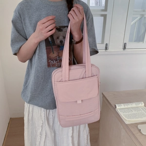 Detail of light pink nylon shoulder bag showing functional front pocket and minimalist design