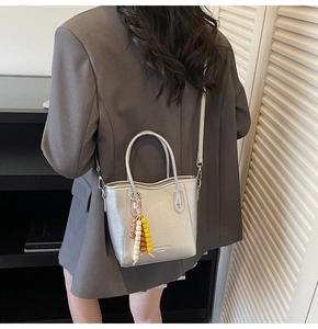 Rear view of model carrying silver metallic bucket bag with colorful bead charm