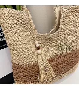 Detailed close-up of woven straw tote bag featuring contrast colors and tassel pendant