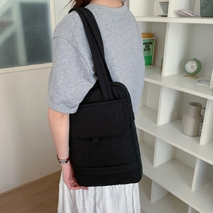 Detail of the large front flap pocket and sturdy wide shoulder strap on a black nylon tote