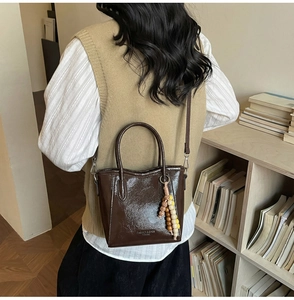 Dark brown patent leather bucket bag with thin strap and colorful beaded charm