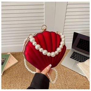 Detail of red shell evening bag featuring large pearl handle and elegant gold clasp