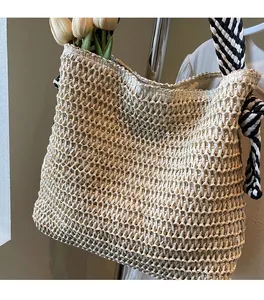 Detail of beige woven straw shoulder bag with checkerboard strap and decorative side knot