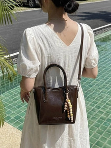 Deep brown glossy leather bucket bag with wooden beads and a long shoulder strap