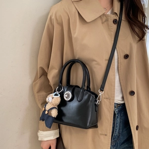 Detail of black handbag featuring a silver twist lock and cute teddy bear pendant