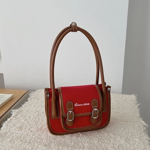 Détail du sac en toile rouge avec bordures en cuir marron et boucles sur tapis en peluche