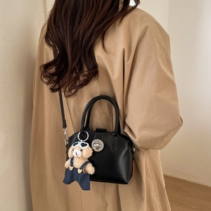 Detail of a black leather handbag with metal turn-lock and cute teddy bear charm on a model