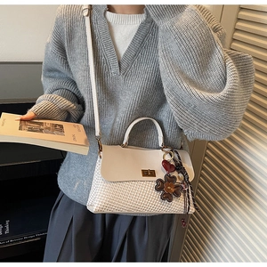 Détail du sac crème avec texture tressée, fermoir doré et pendentif fleur élégant