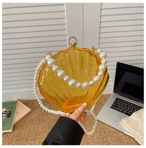 Detailed macro of amber shell-shaped acrylic clutch with pearl handle and golden clasp