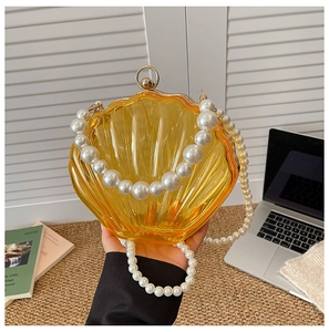 Detail of yellow shell-shaped acrylic evening bag with faux pearl handle and metal clasp