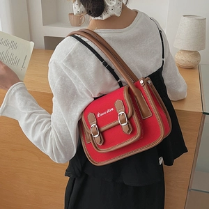 Détail du sac bandoulière en toile rouge avec bordure en cuir marron et boucles