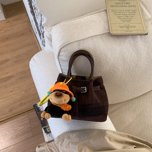 Detail der dunkelbraunen Wildleder-Beuteltasche mit Affen-Plüschtier auf einem Sofa