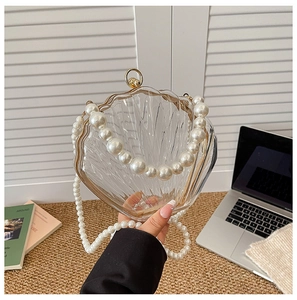 Detail of shell-shaped acrylic clutch with gold metal trim and pearl handle strap