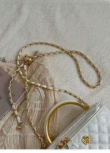 Detail of white quilted leather bag with gold camellia clasp and round metal handle