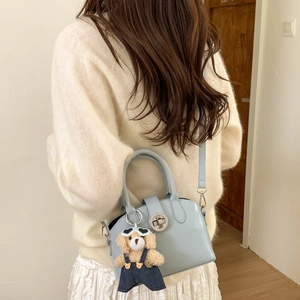 Close-up of light blue mini handbag featuring a metal twist lock and cute teddy bear charm