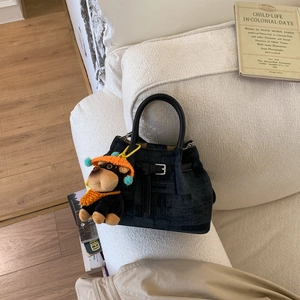Detailansicht der dunklen Eimertasche mit Affen-Plüschanhänger auf dem Stoffsofa