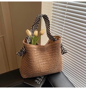 Détail d'un sac cabas en paille tissée avec anses rayées et tulipes sur un banc en cuir