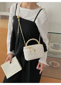Detail of white quilted box bag with gold flower logo and metal handle on model
