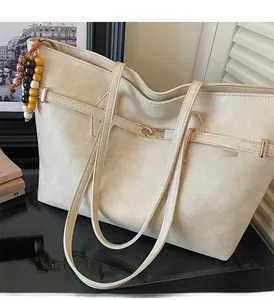 Detail of a beige tote bag showing textured leather, gold buckle and bead charm