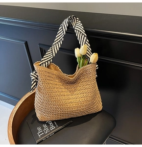 Détail d'un cabas en paille tissé avec bandoulière à rayures noires et blanches sur une chaise