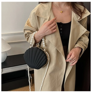 Detailed view of shell-shaped acrylic evening bag with white pearl strap and gold hardware