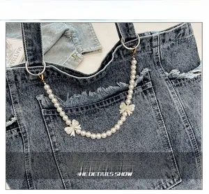 Close-up of vintage denim tote bag with frayed edges, pearl chain and white bows