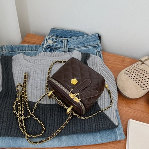 Detail of dark brown quilted chain bag with rabbit ear zipper and gold floral logo
