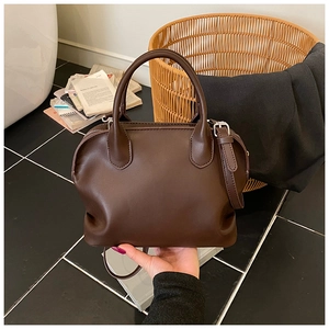 Detailed close-up of dark brown leather shell bag with cylindrical handles and adjustable strap
