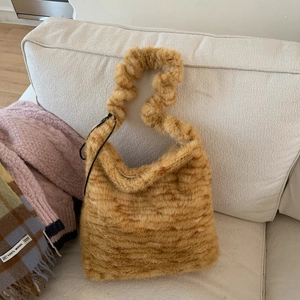 Close-up of ginger plush faux fur bag with a trendy scrunchie handle on white sofa