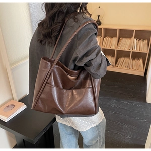 Modella con borsa tote grande marrone scuro in ecopelle lucida in una libreria urbana