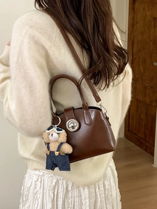 Brown retro shoulder bag with a bear charm, shown from a side view on a model