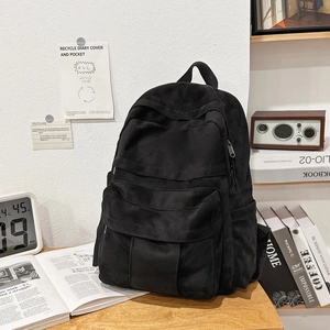 Close-up of a black canvas backpack on a vintage wooden desk with books and accessories