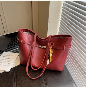Close-up of a burgundy tote bag with wood bead tassel and subtle litchi grain texture