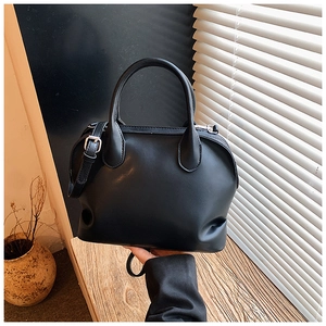 Close-up of minimalist black leather shell bag with sturdy dual handles and silver hardware