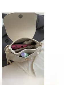 Détail de l'espace de rangement interne du sac selle en simili cuir crème avec objets