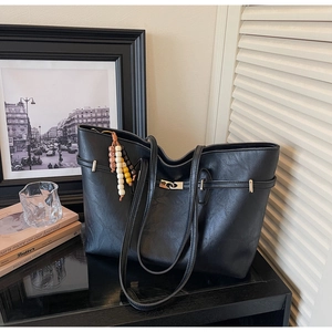 Close-up of black leather tote bag featuring a silver twist-lock and wood bead tassel
