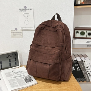Detail view of the dark brown suede backpack on a desk showing its side pocket