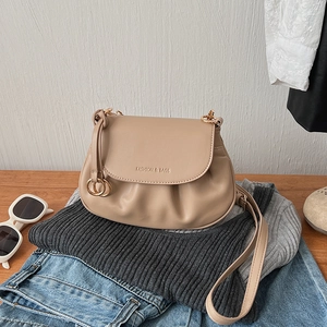 Close-up of beige pleated PU leather bag with gold buckle on casual clothing background