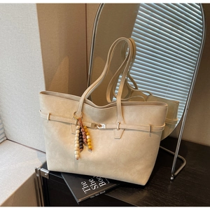 Detail of a beige tote bag with metallic buckle, matte finish and colorful beaded charm