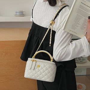 Detail view of quilted white vanity bag with golden camellia and chain strap