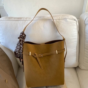 Close-up of tan faux leather bucket bag with decorative scarf on a white sofa