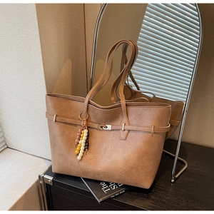 Close-up of brown faux leather tote bag with metallic buckle and beaded charm