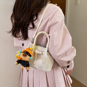 Detail der beigen strukturierten Eimertasche mit Zierschnalle und Plüschhund-Anhänger