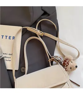 Close-up of beige shoulder bag with adjustable strap and plush bear charm on a suit