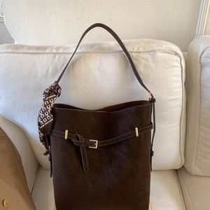Close-up of a dark brown suede bucket bag with decorative scarf and golden buckle