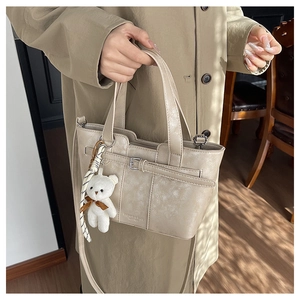 Detail der beige Beuteltasche mit Lederstruktur und süßem weißem Plüschbär-Anhänger