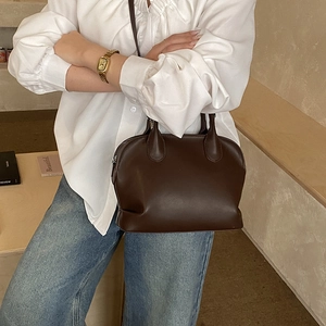 Deep brown leather boston bag shown being worn cross-body against a minimalist background