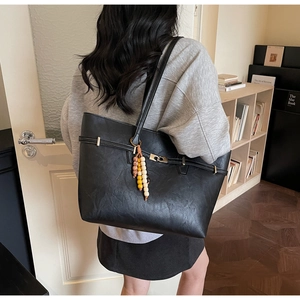 Detail of black faux leather tote bag featuring gold buckle and colorful beaded keychain