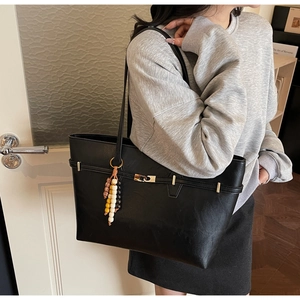 Detail of black tote bag featuring matte leather texture and beaded charm accessory