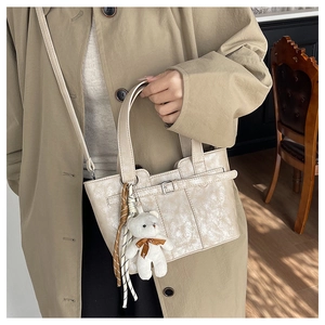 Detail der beigen glänzenden Beuteltasche mit Bärenanhänger und gewebten Riemen am Outfit
